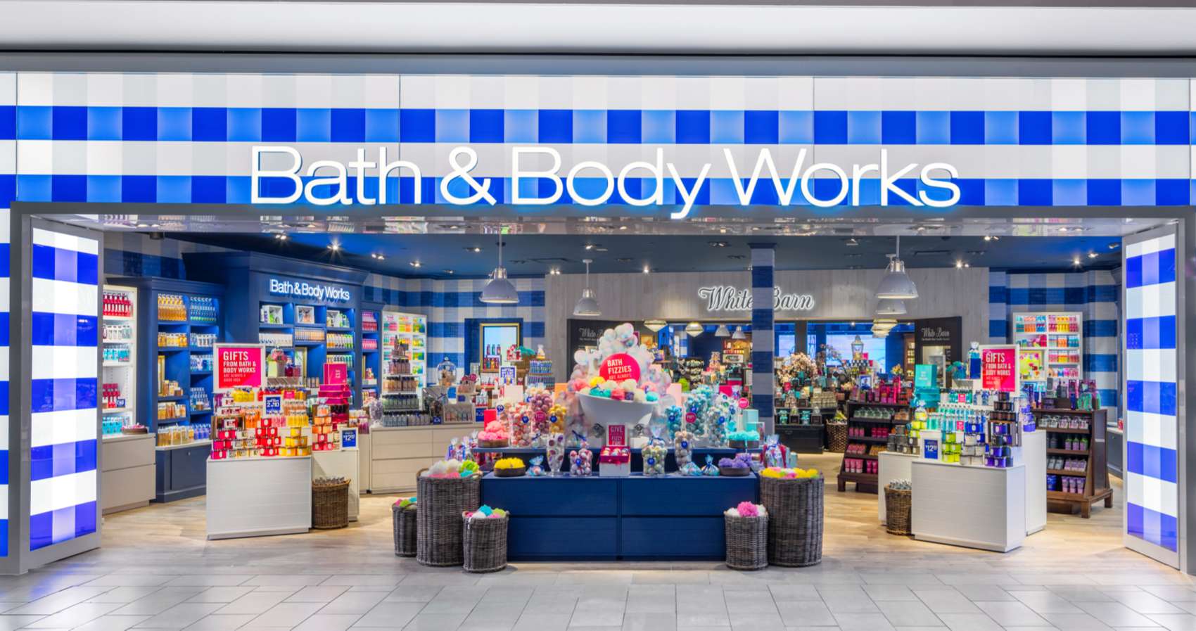 A well light, Bath and Body Works storefront with displays arranged neatly to showcase the products that span from left to right with Bath and Body Works signage above at the entrance.