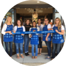 bbw-cws-home-roundimage-stores A diverse team of Bath and Body Works employees wearing their uniformed blue aprons holding a blue ribbon together in front of a new store location.