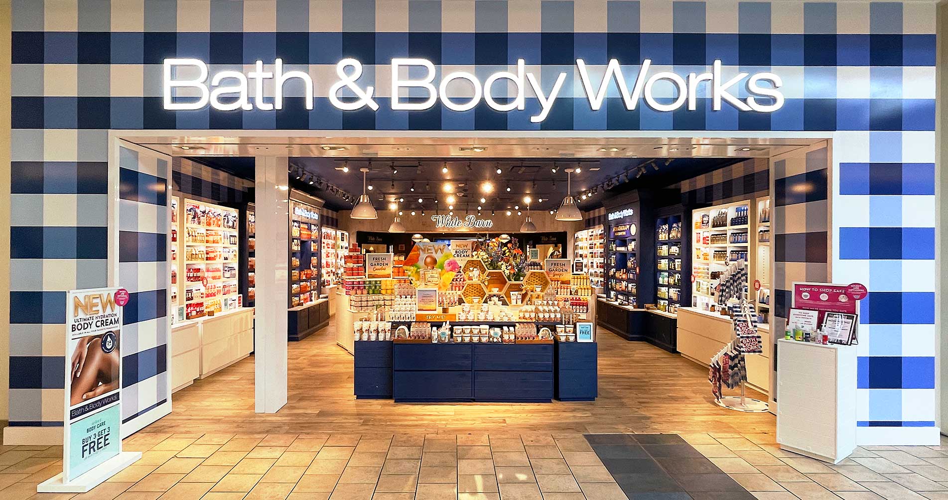 A well light, Bath and Body Works storefront with displays arranged neatly to showcase the products that span from left to right with Bath and Body Works signage above at the entrance.